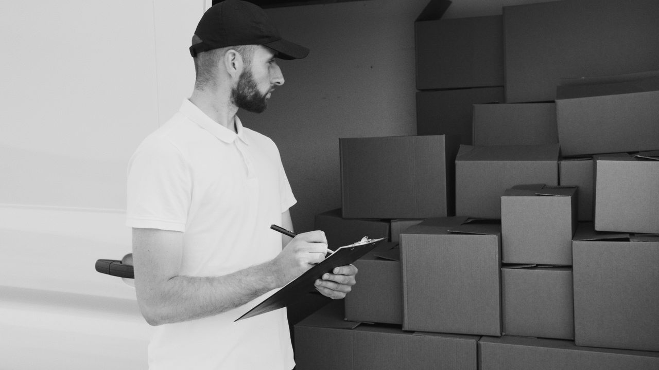 services-08 A delivery man inspecting cardboard boxes in a van, preparing for shipment.